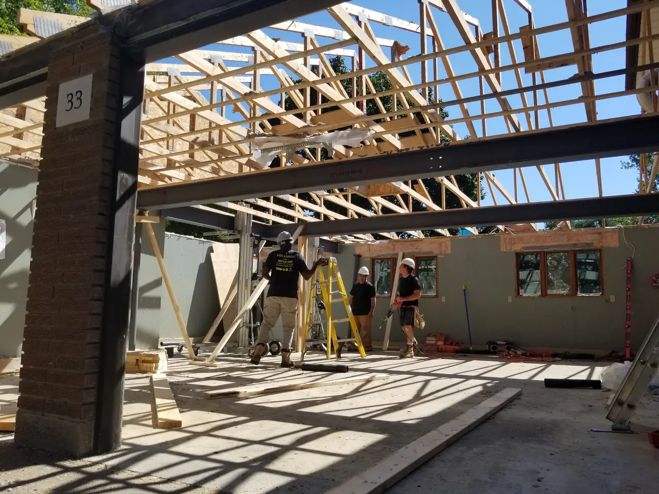 Second-storey addition under construction: steel beams and new roof trusses in place above the existing walls, with the crew on site.
