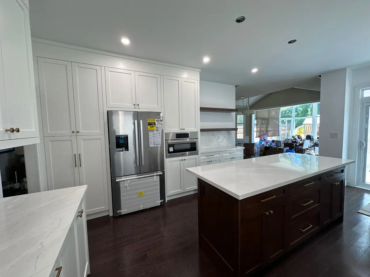 White shaker kitchen with a dark-stained island and quartz counters opening into a vaulted family room.