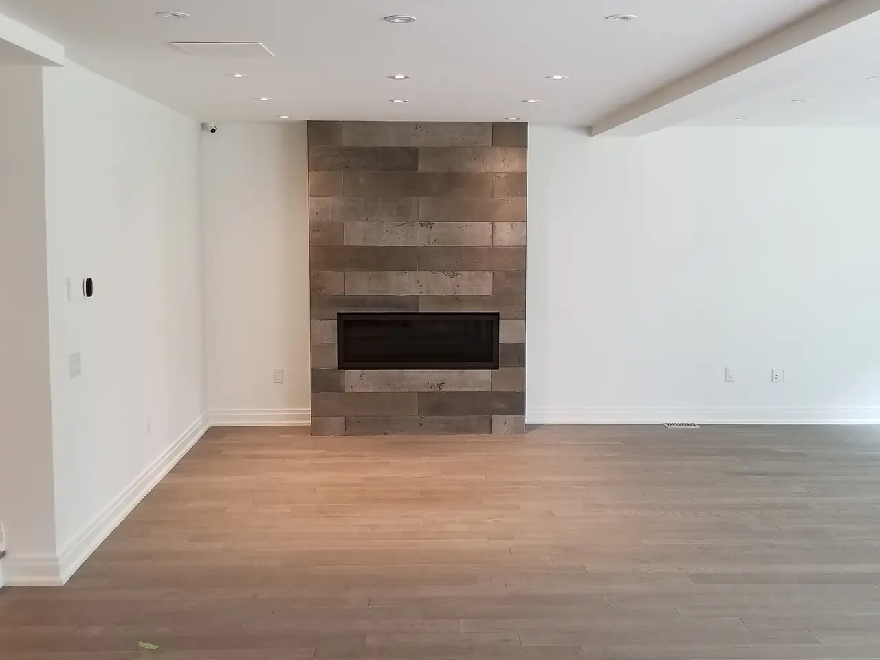 Living room after a whole-home renovation: a linear fireplace set into a full-height tiled feature wall, pot lights and new oak flooring.