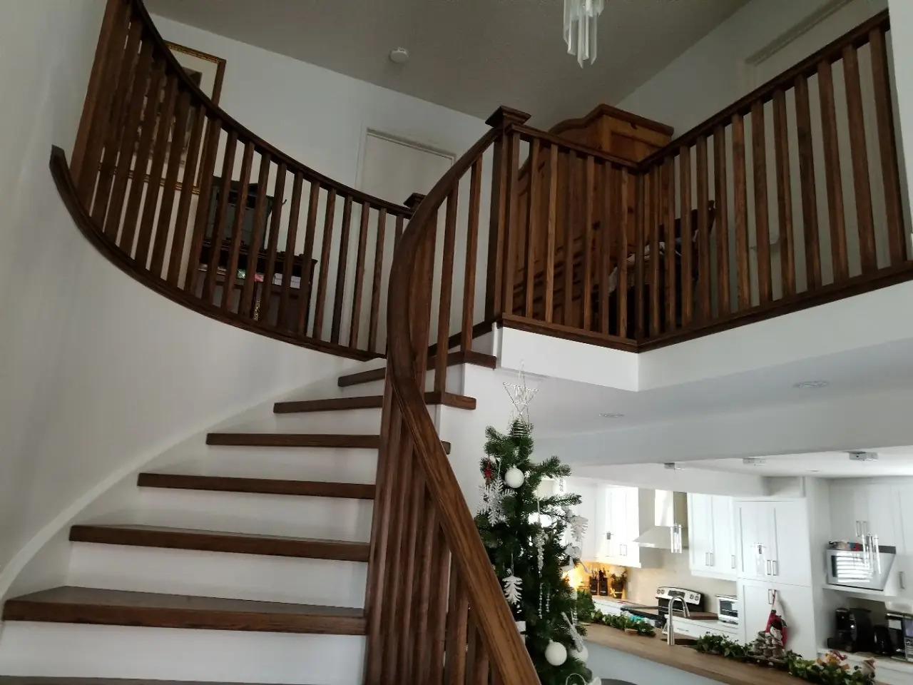 Curved oak staircase and upper-landing railing in a whole-home renovation, with the new white kitchen visible below.