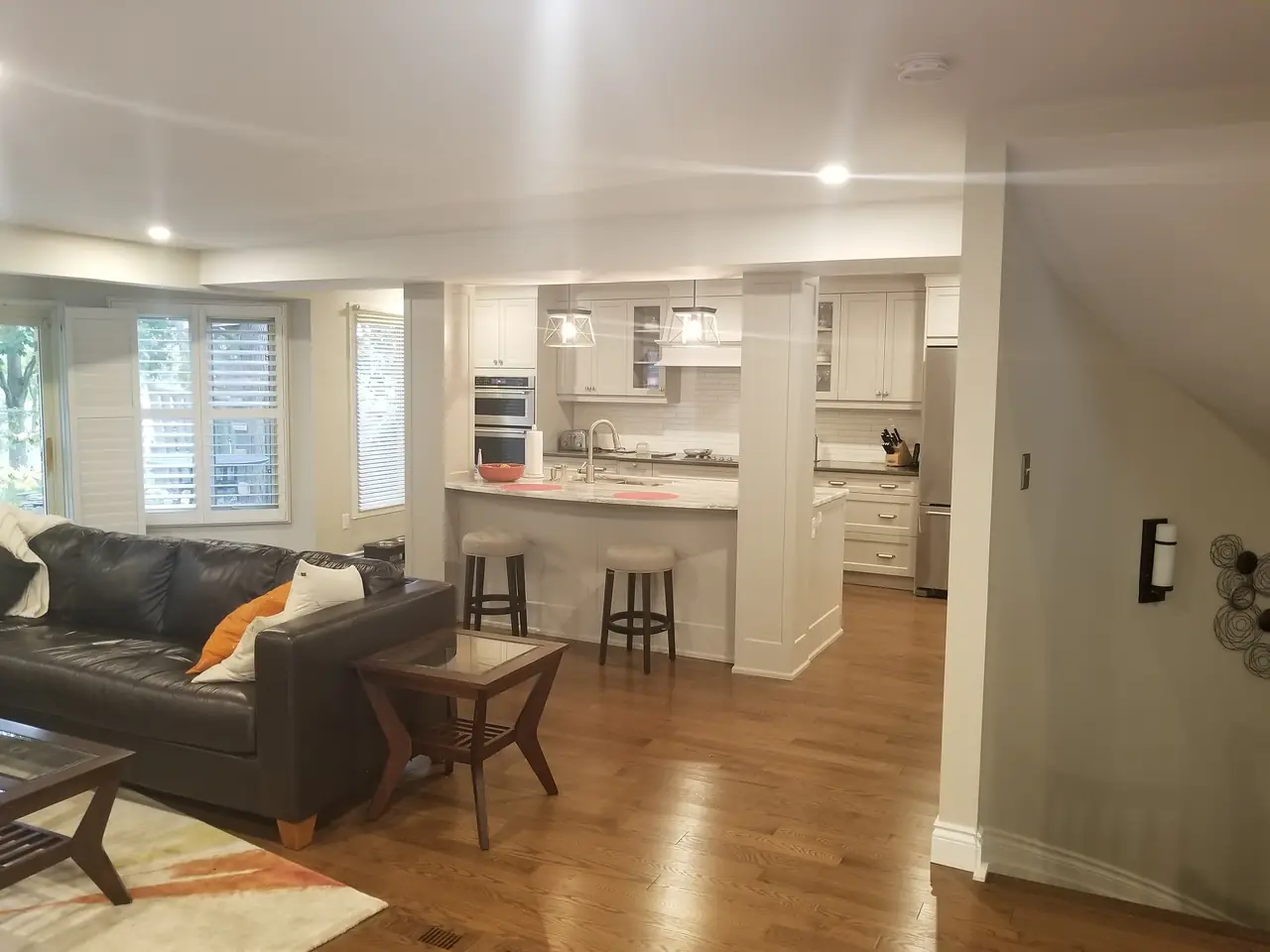Main-floor renovation with a white kitchen and quartz peninsula opening onto the living room, with structural posts finished to match the trim.