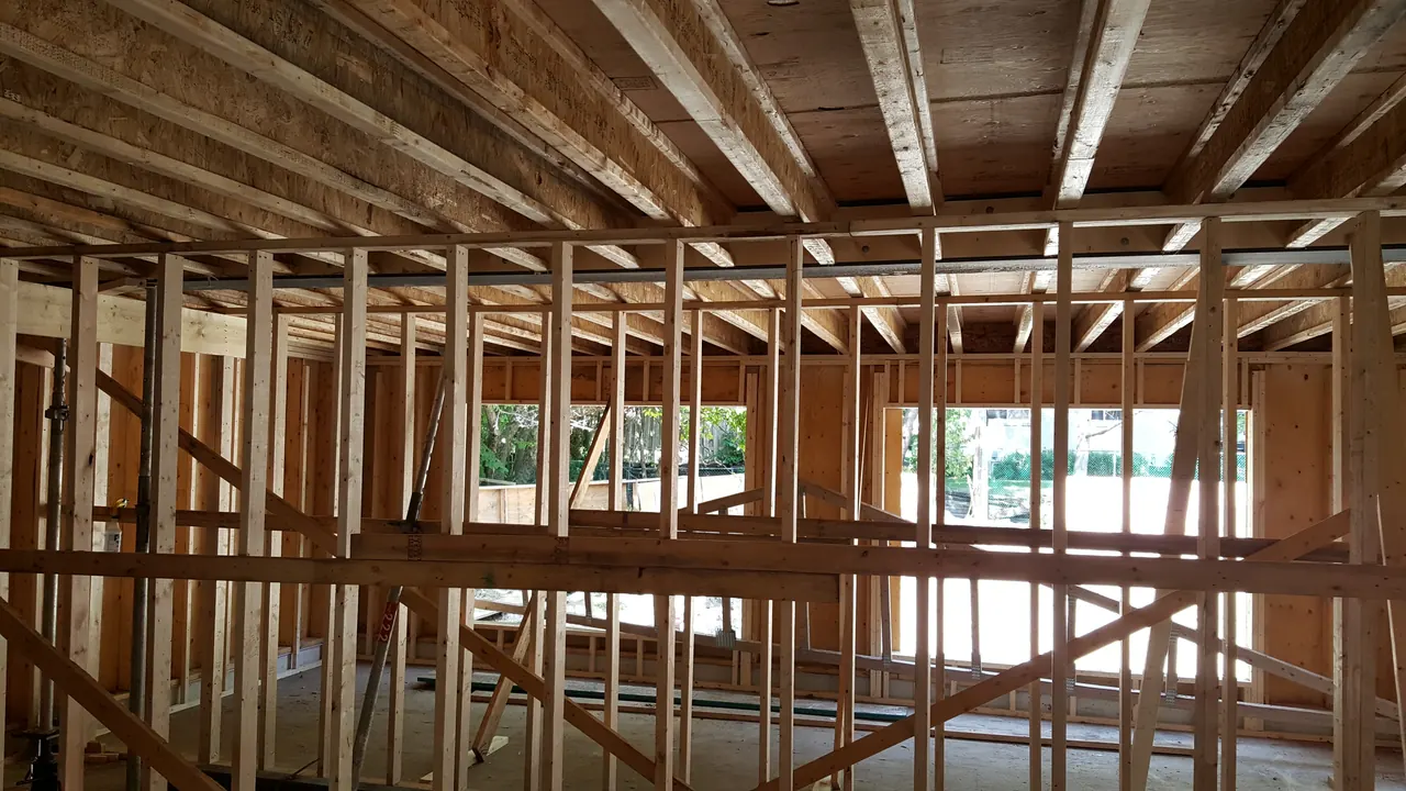 Interior framing of a new upper storey, with engineered floor joists overhead and sunlight through the new window openings.