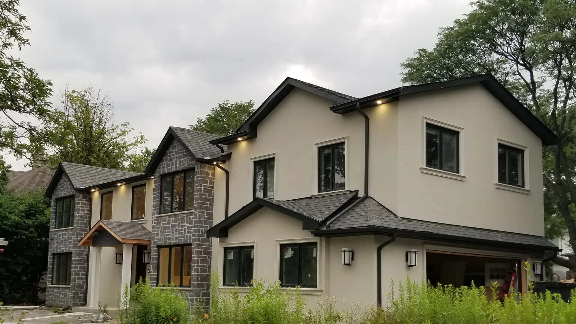 Finished whole-home renovation with a grey ledgestone and cream stucco exterior and black-framed windows, built by MATCON INC.