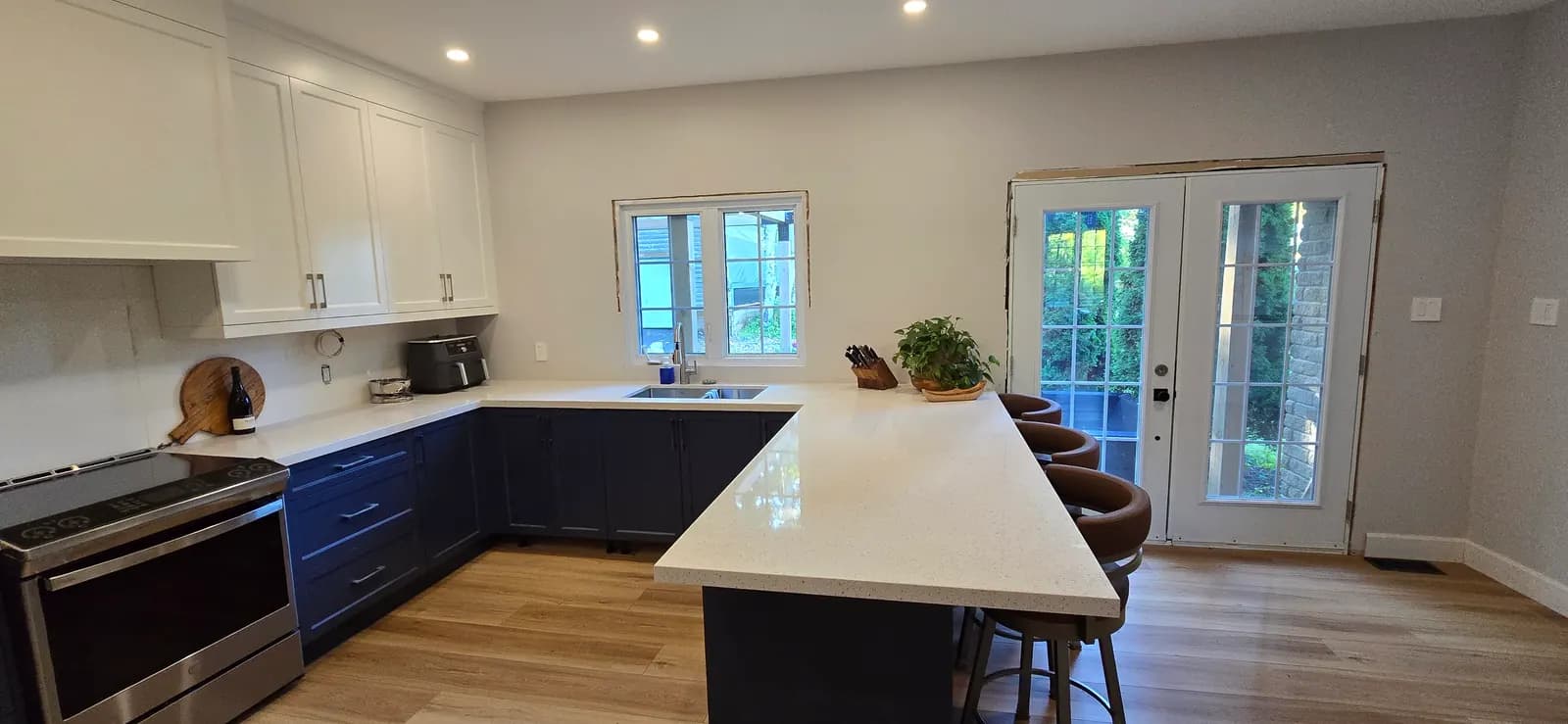 After the renovation: an open main floor with a navy and white kitchen, quartz peninsula and French doors to the deck.