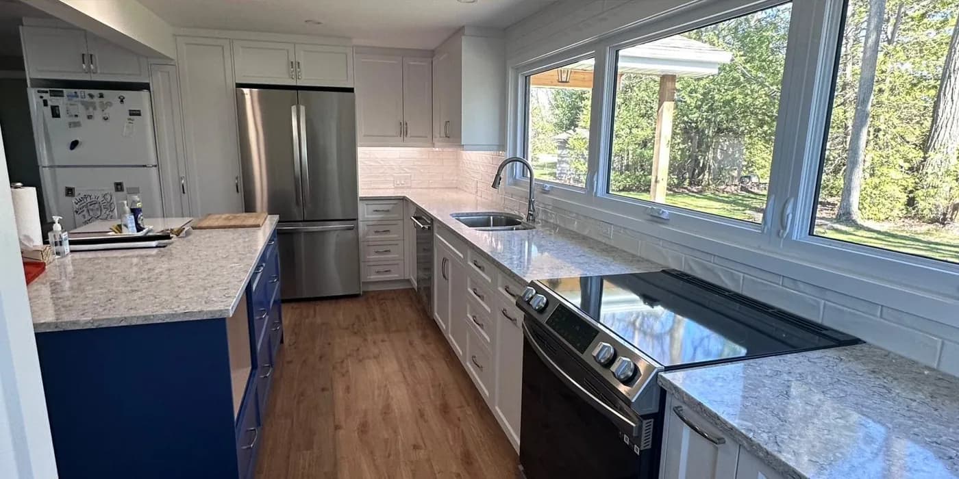 The same kitchen after the renovation: white shaker cabinets, a navy island, quartz counters and new flooring.