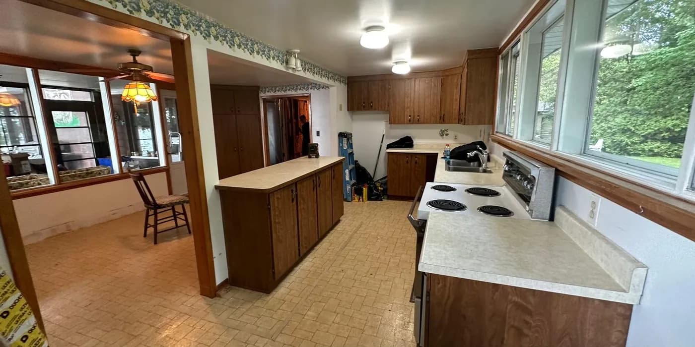 The original kitchen before a whole-home renovation: dark wood cabinets, a coil-top range and patterned vinyl flooring.